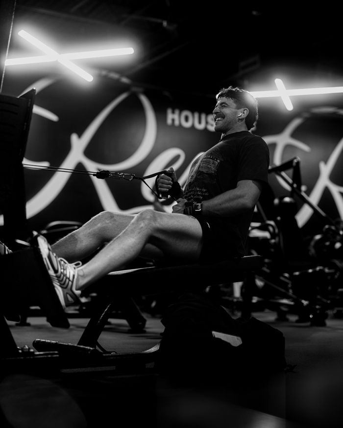 Black and white photo of a man using a rowing machine in a modern gym setting.