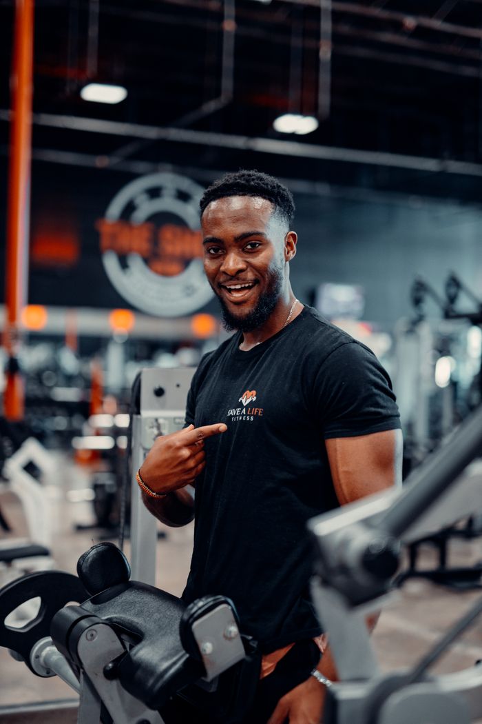 fitness-service-01 Confident man at the gym pointing to his fitness shirt, showcasing enthusiasm for workout.
