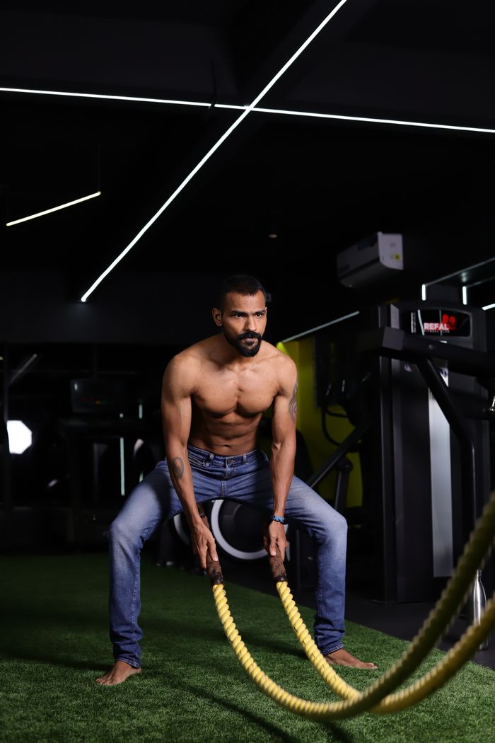 A muscular man engages in a battle rope workout indoors, highlighting strength and fitness.